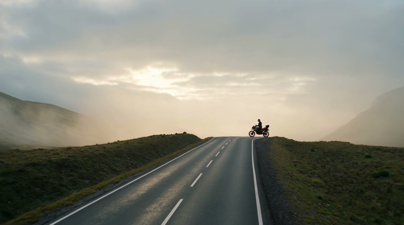 A rider silhouetted on a mountain road at first light, from the opening film